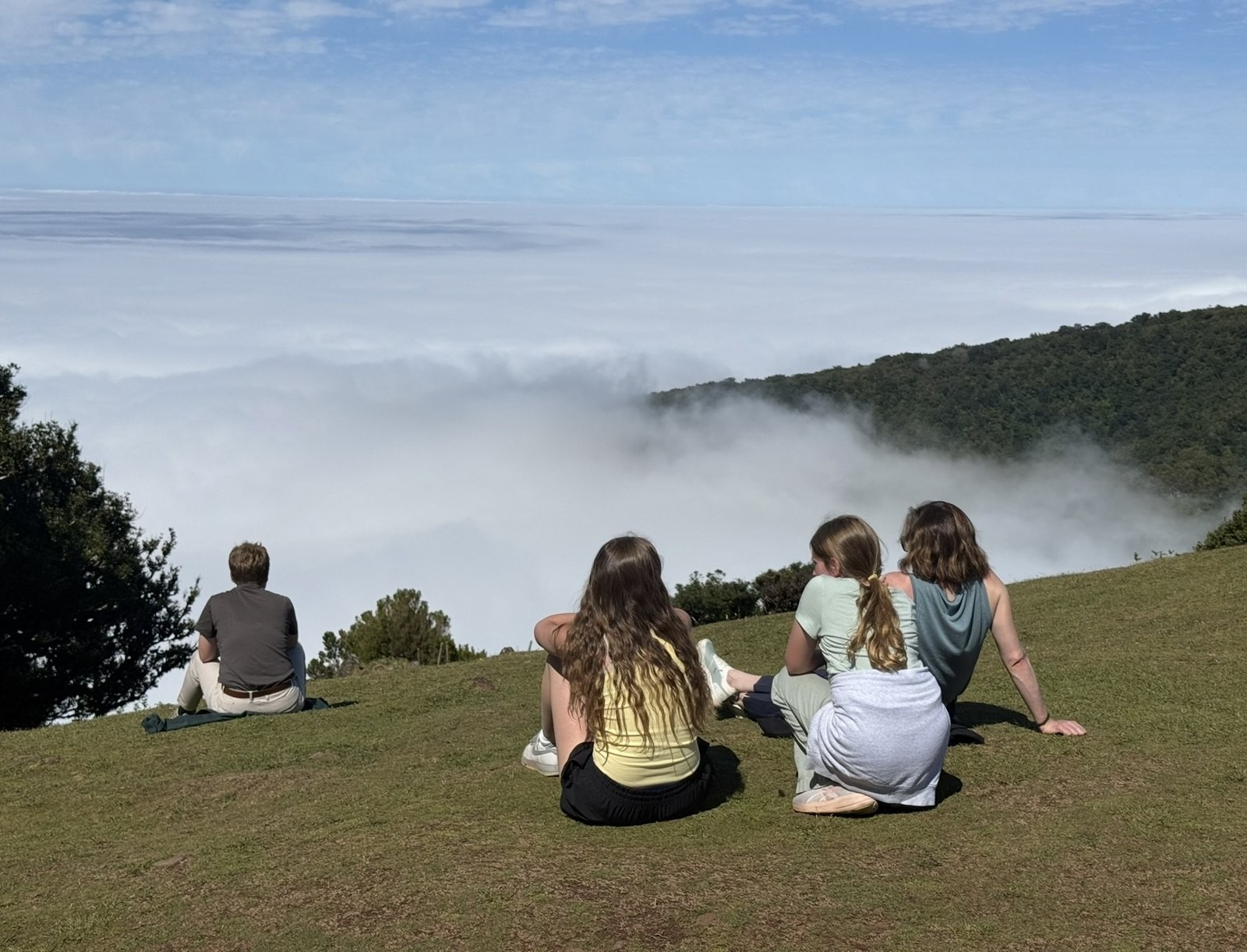 Dan’s family sitting on a grassy hillside looking out over a sea of clouds in Madeira, Portugal